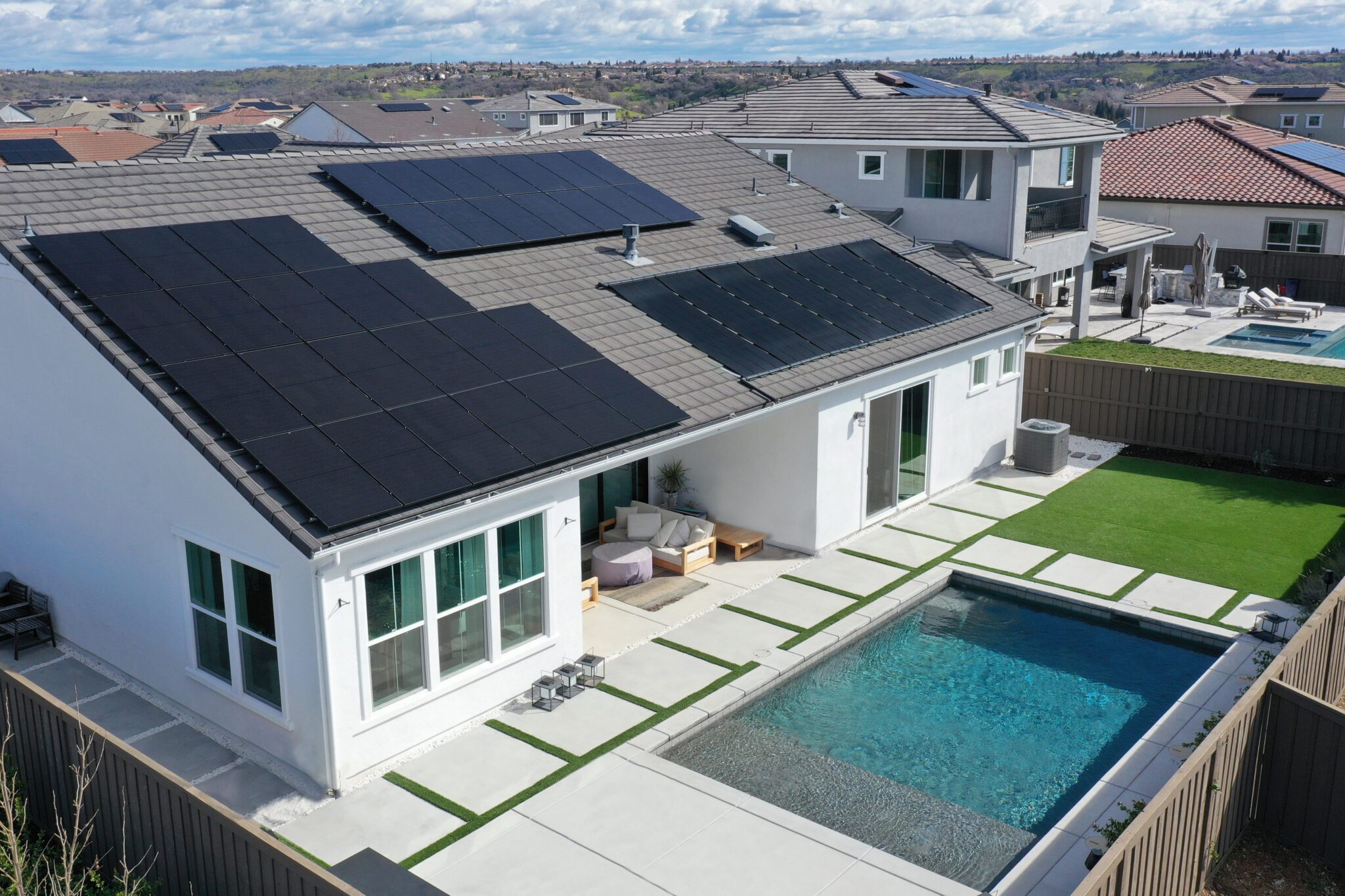 Aerial view of a modern home with rooftop solar panels and a backyard pool